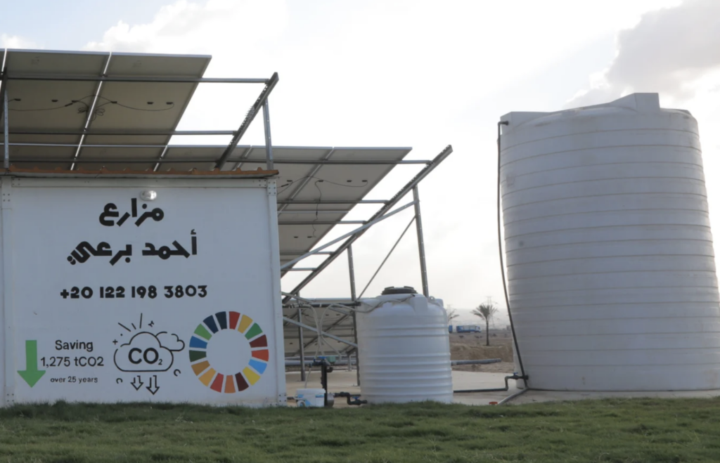Solar panels and white water tanks at the site labeled "Mazare3 Ahmed Brei" in Egypt, promoting CO2 savings over 25 years. A step towards addressing water scarcity, proudly backed by NoorNation.
