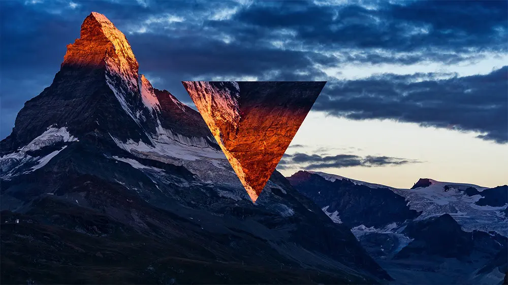 A mountain peak at sunset, with a triangular section inverted showing a different sky and mountain lighting.